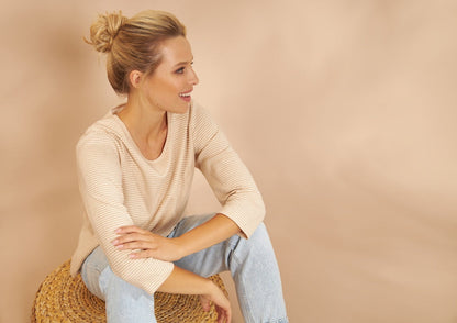 eine sitzende Frau die das naturbelassene Shirt mit dreiviertel Arm NATIVO in der Farbe Ivory Beige trägt